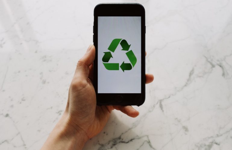 From above view of faceless person holding mobile phone with white screen and green recycle logo above marble surface