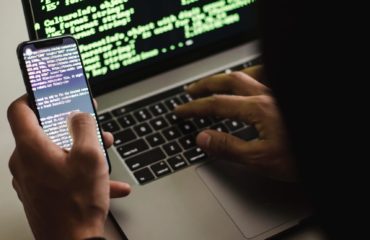 Free Unrecognizable hacker with smartphone typing on laptop at desk Stock Photo