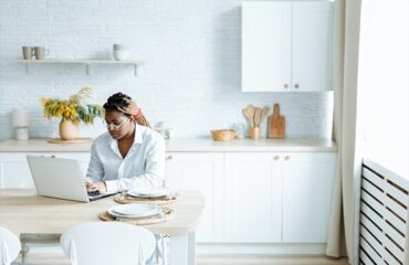 Woman Typing on a Laptop While in the Kitchen